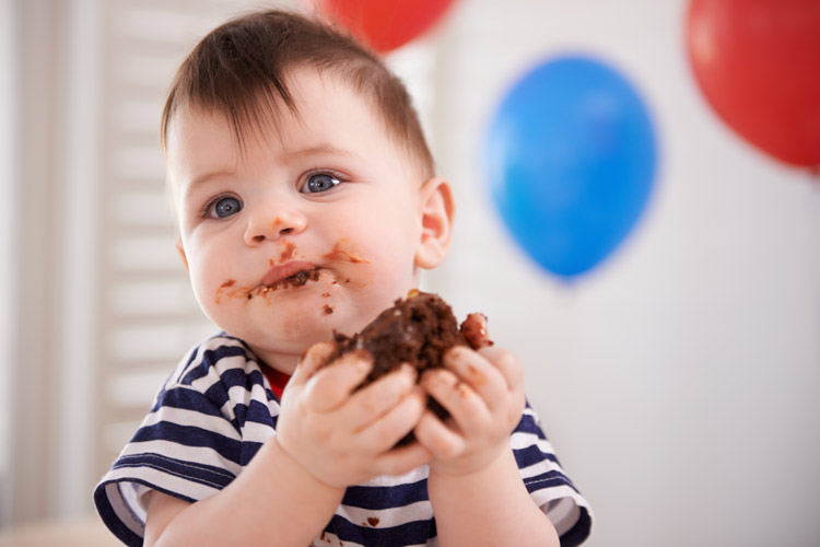 A messy baby eating a piece of chocolate cake