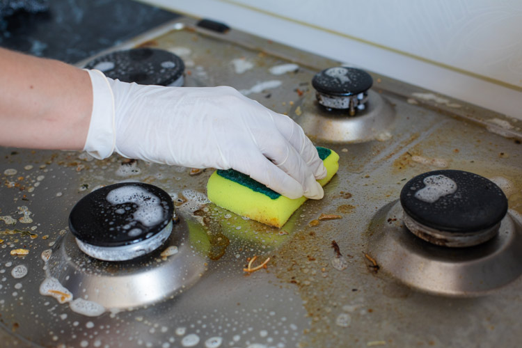 Person cleaning stove with sponge