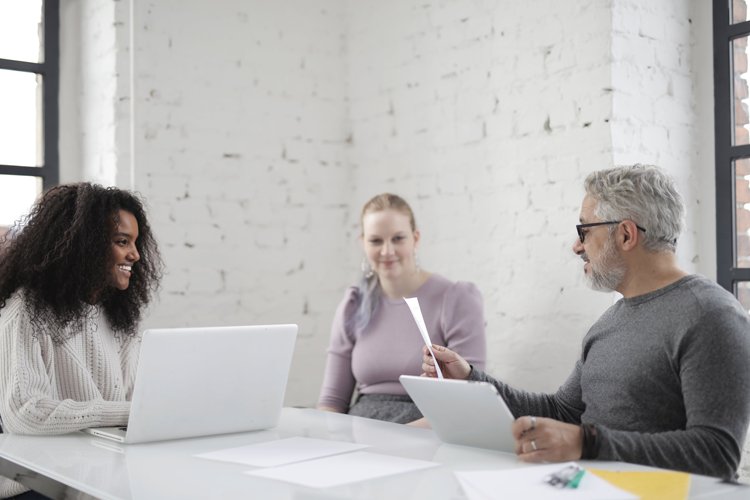 Three people talking in a white brick conference room