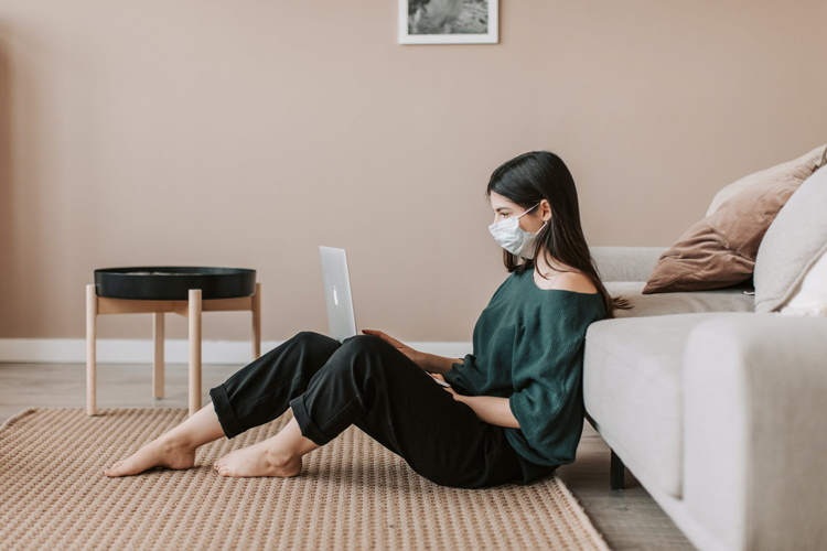 Woman wearing a mask while sitting on the floor with her laptop.
